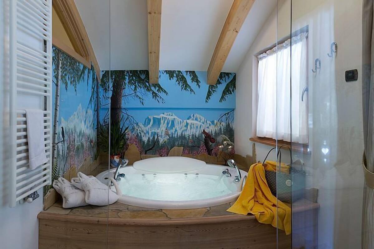Un baño con una bañera grande, vigas de madera y un mural de un paisaje montañoso.