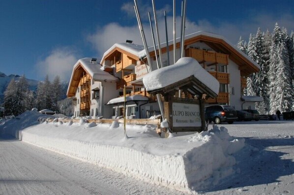 A hotel with a wooden facade, a signboard, and snow-covered surroundings. - Lupo Bianco Wellness & Walking Hotel (Canazei)