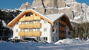Una chaleta de varios pisos con techo inclinado, balcones de madera y vistas a montañas nevadas.
