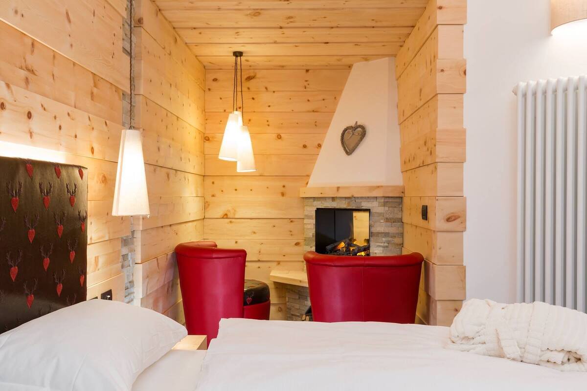 Una habitación acogedora con paredes de madera, chimenea, una cama y sillas rojas.