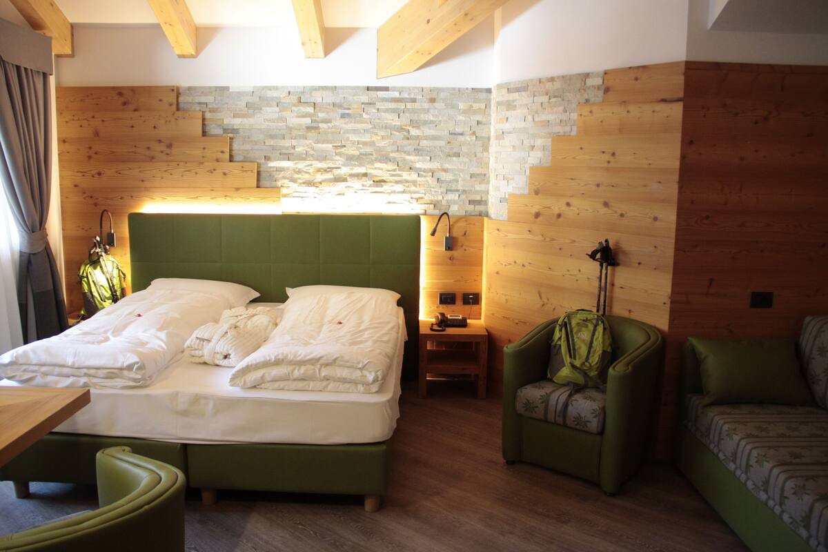Un dormitorio con una cama grande, un sillón verde, un cabecero de madera y una pared de piedra.