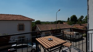 A balcony with a wooden table and chairs, a white van, and a building with a tiled roof in the background. - Rebetika Hotel (Selçuk)