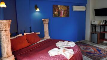 A room with a bed, a wall-mounted TV, a small cabinet, and a decorative pillar.