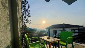 A balcony with a wooden table and two green chairs, overlooking a residential area with a view of the sun setting behind a building. - Rebetika Hotel (Selçuk)