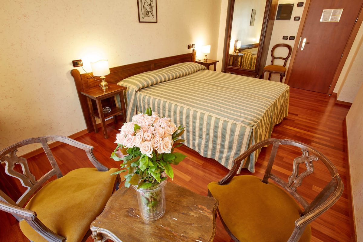 Una camera d'albergo con un letto, due poltrone, un tavolo con un vaso di fiori e un pavimento in legno.