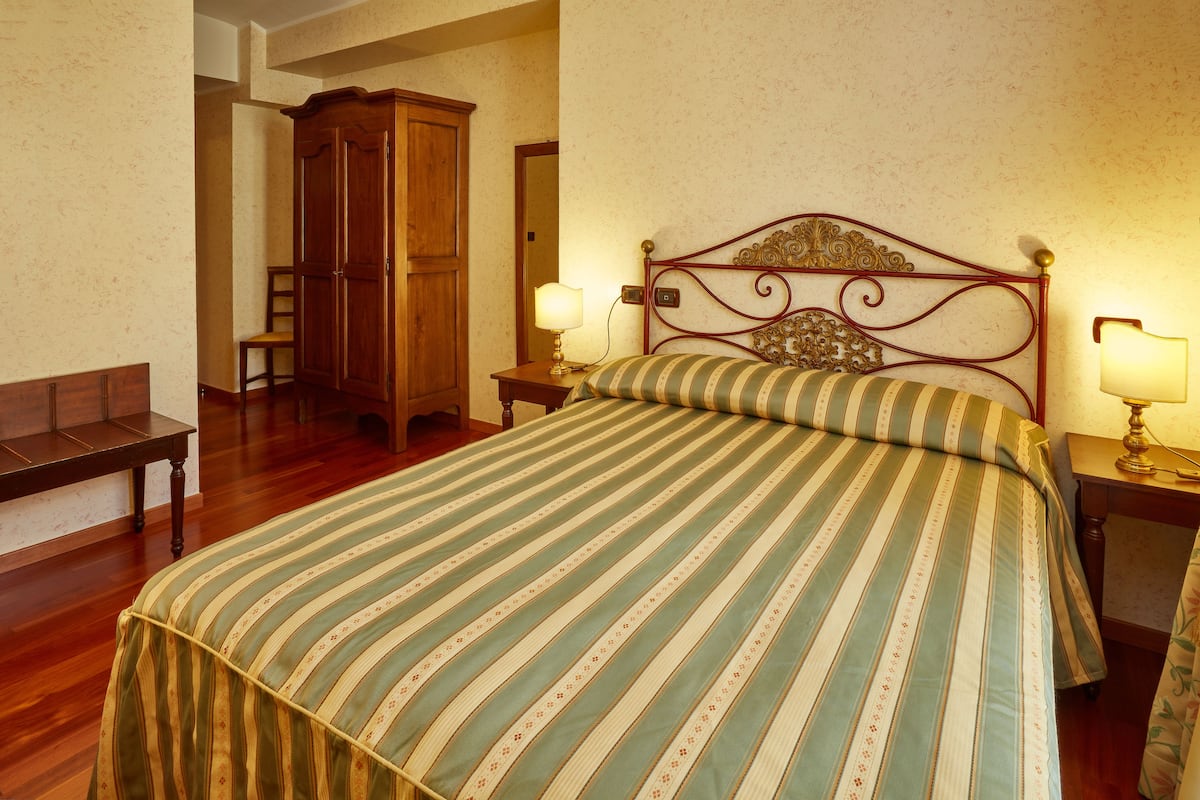 Un letto rifatto con cura, coperta a righe, testiera in legno e due abat-jour.