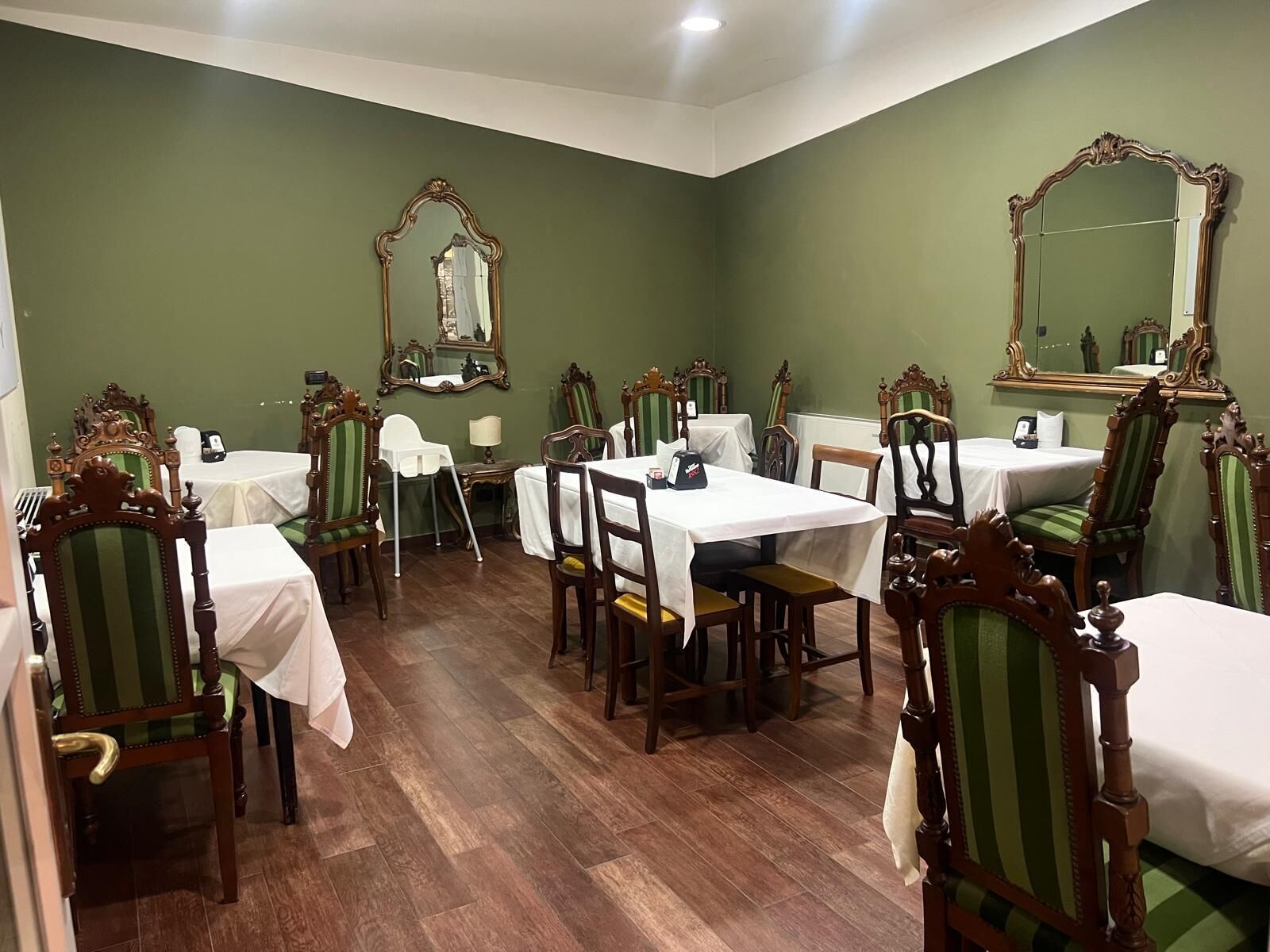 Comedor con paredes verdes, sillas de madera y mesas dispuestas para comer.