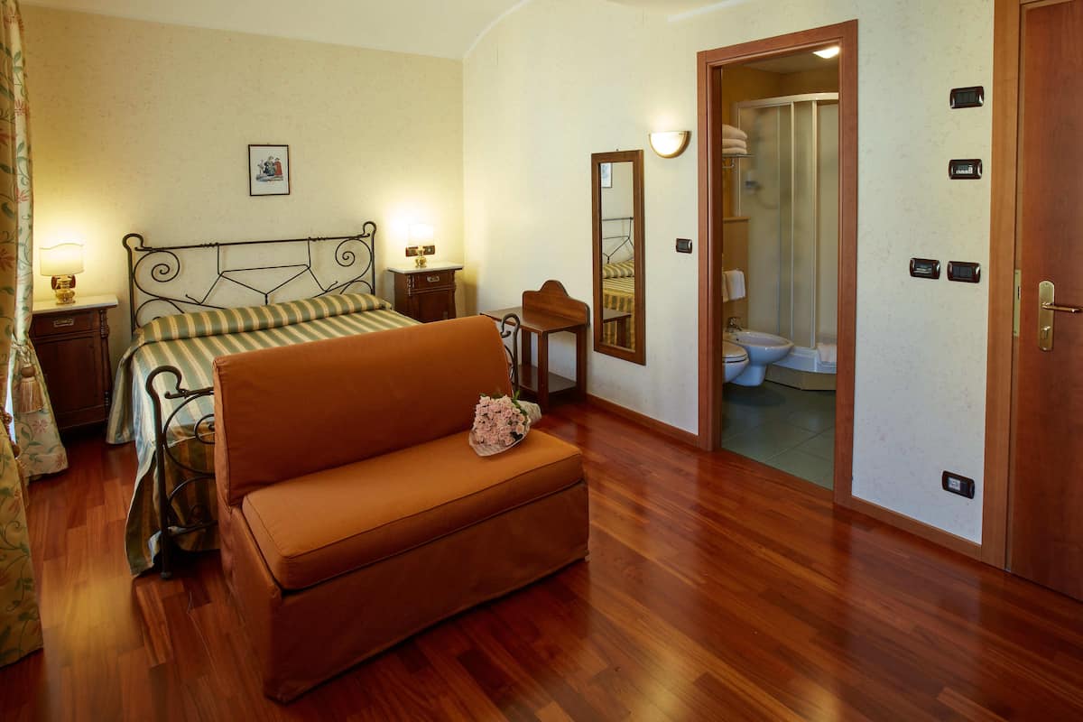 Una camera da letto con un letto, un divano, un comodino, uno specchio e un bagno visibile attraverso una porta aperta.