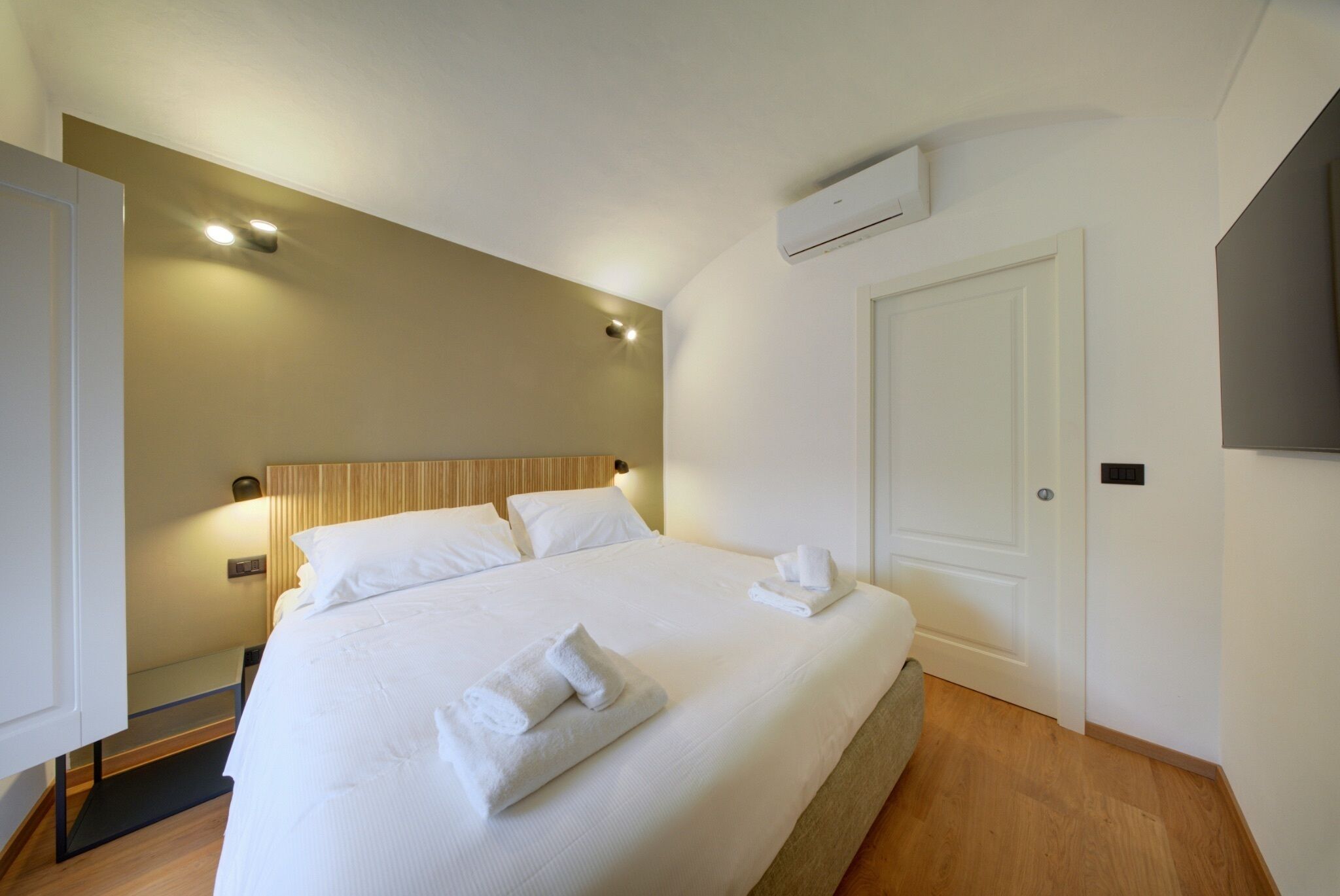 Un letto rifatto con lenzuola e asciugamani bianchi, un comodino con una lampada e un condizionatore d'aria a parete.