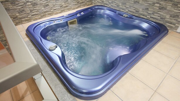 Un jacuzzi con un muro de piedra de fondo y suelo de baldosas.