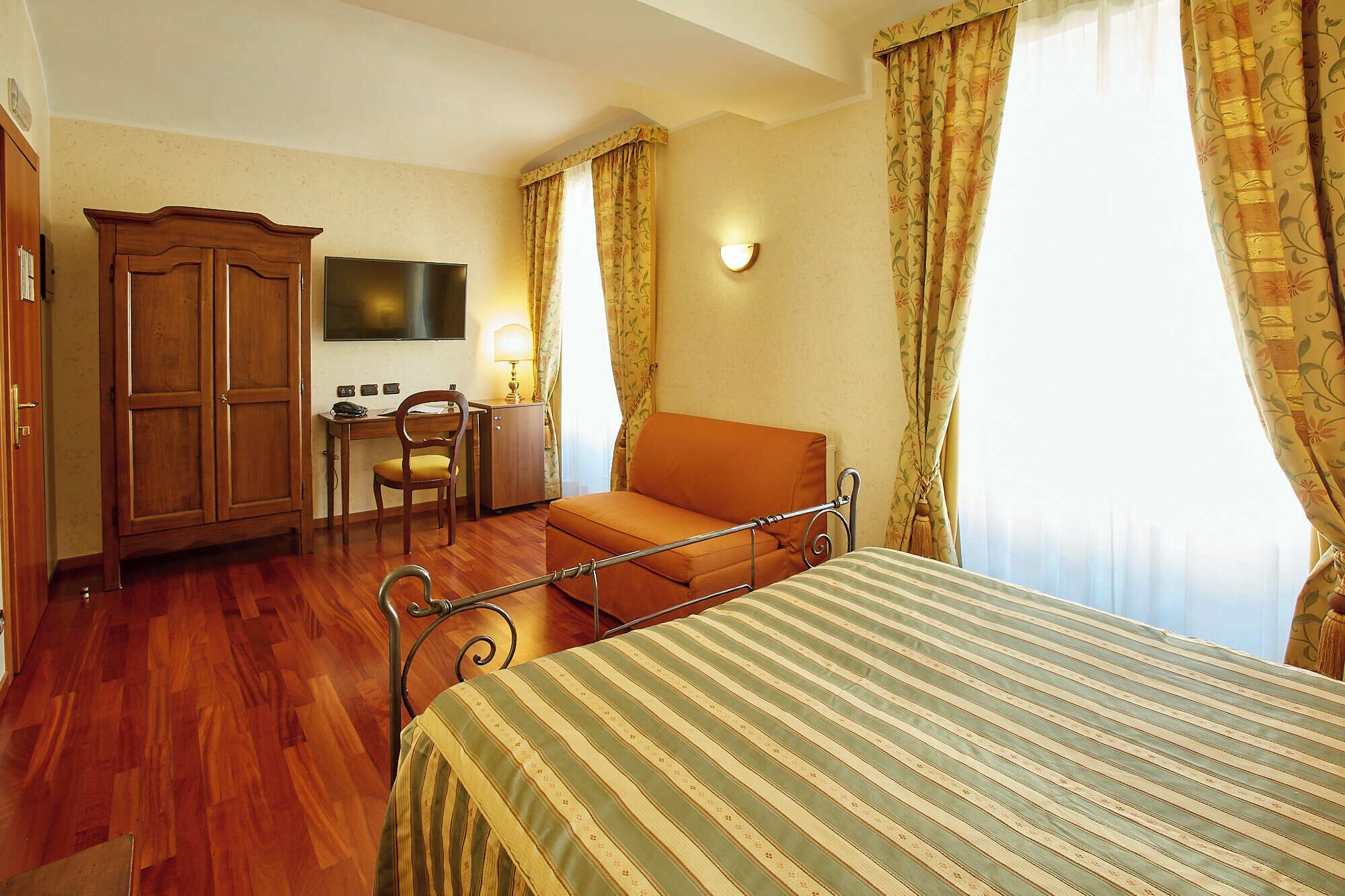 A hotel room with a bed, a desk, a chair, a wardrobe, and a television.