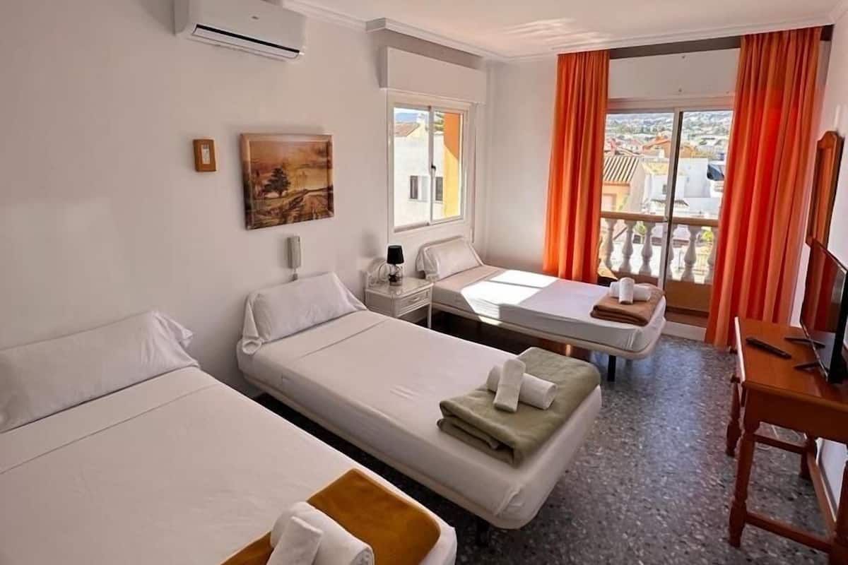 A hotel room with two beds, a desk, a chair, and a balcony with orange curtains.