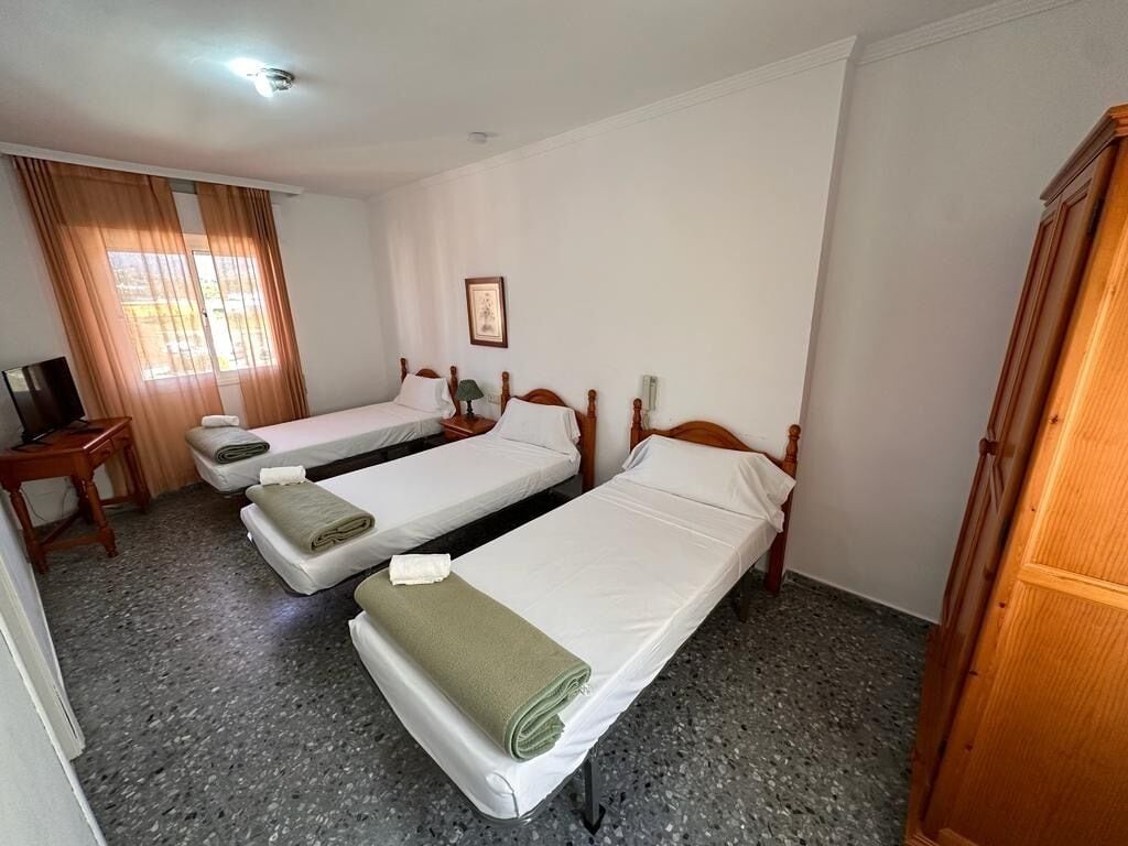 A hotel room with three single beds, a desk with a chair, a wardrobe, and a framed picture on the wall.