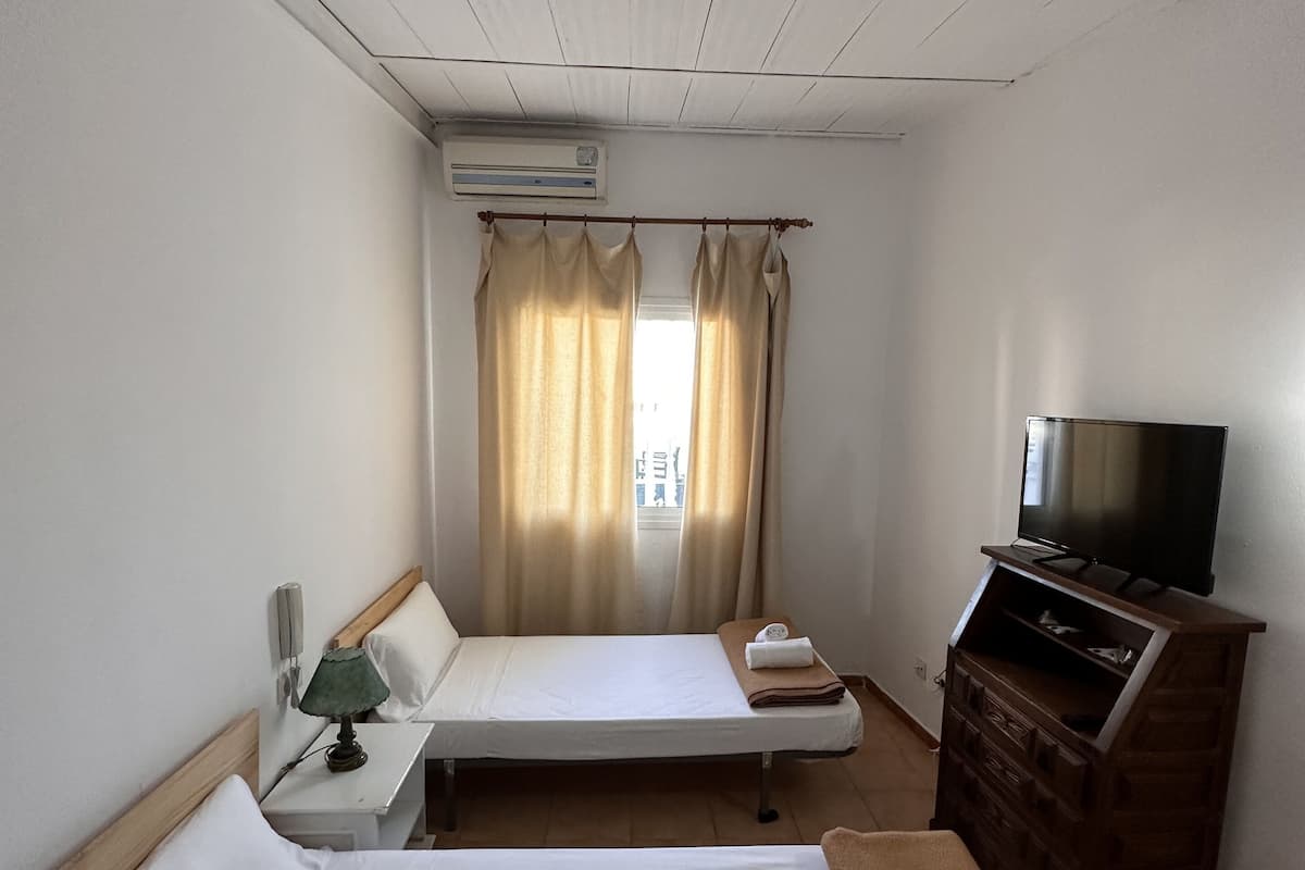 A hotel room with a bed, a TV, a dresser, and an air conditioning unit.