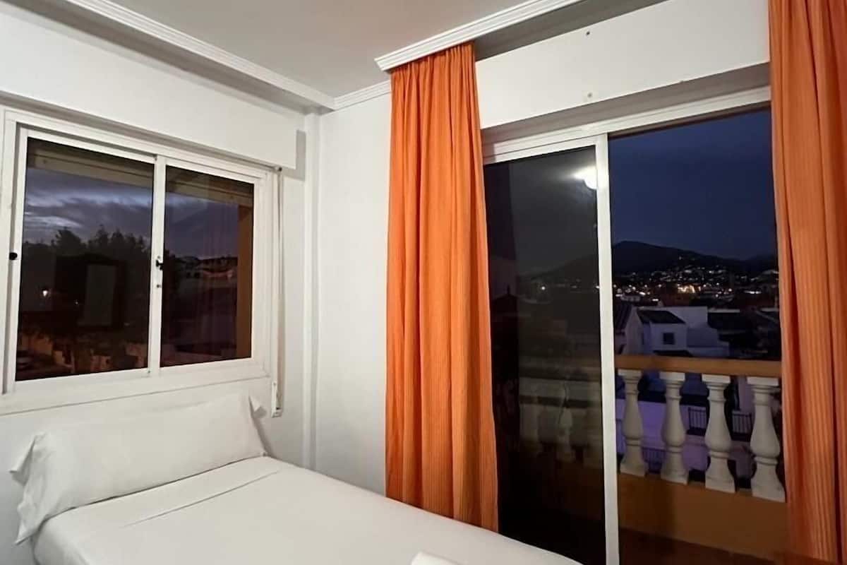 A hotel room with a bed, a window, and a balcony with curtains.