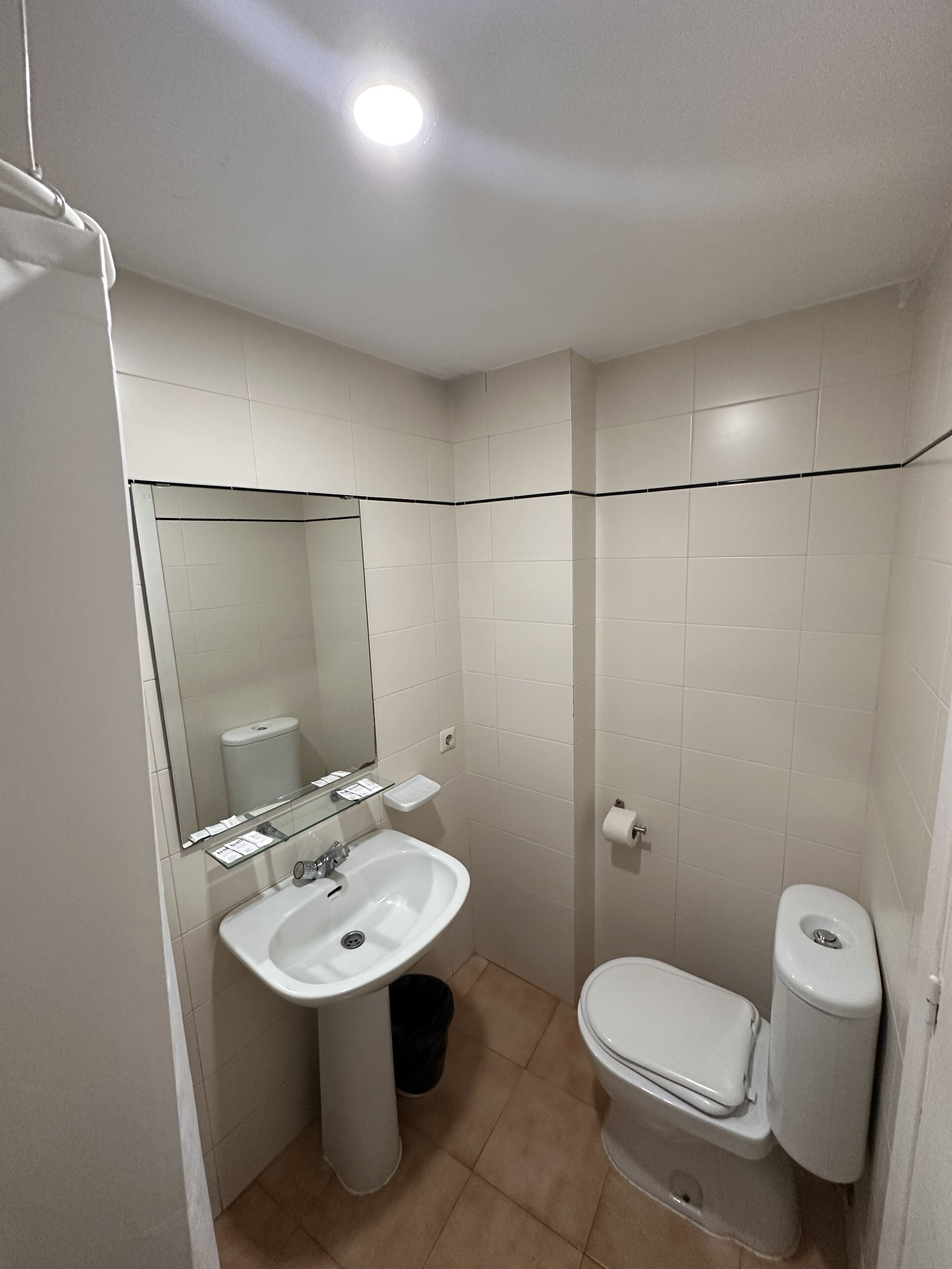 Un baño pequeño y limpio con azulejos blancos, un lavamanos, un inodoro y un espejo.