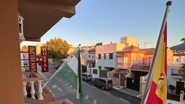 A balcony with a view of a street, a flag, and a sign that reads "SAN FELIPE HOSTA". - Hostal San Felipe (Marbella)