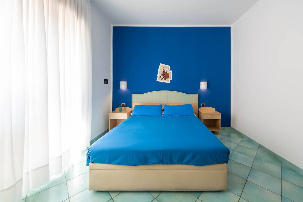 A bedroom with a bed, two bedside tables, a nightstand, and a wall-mounted picture.