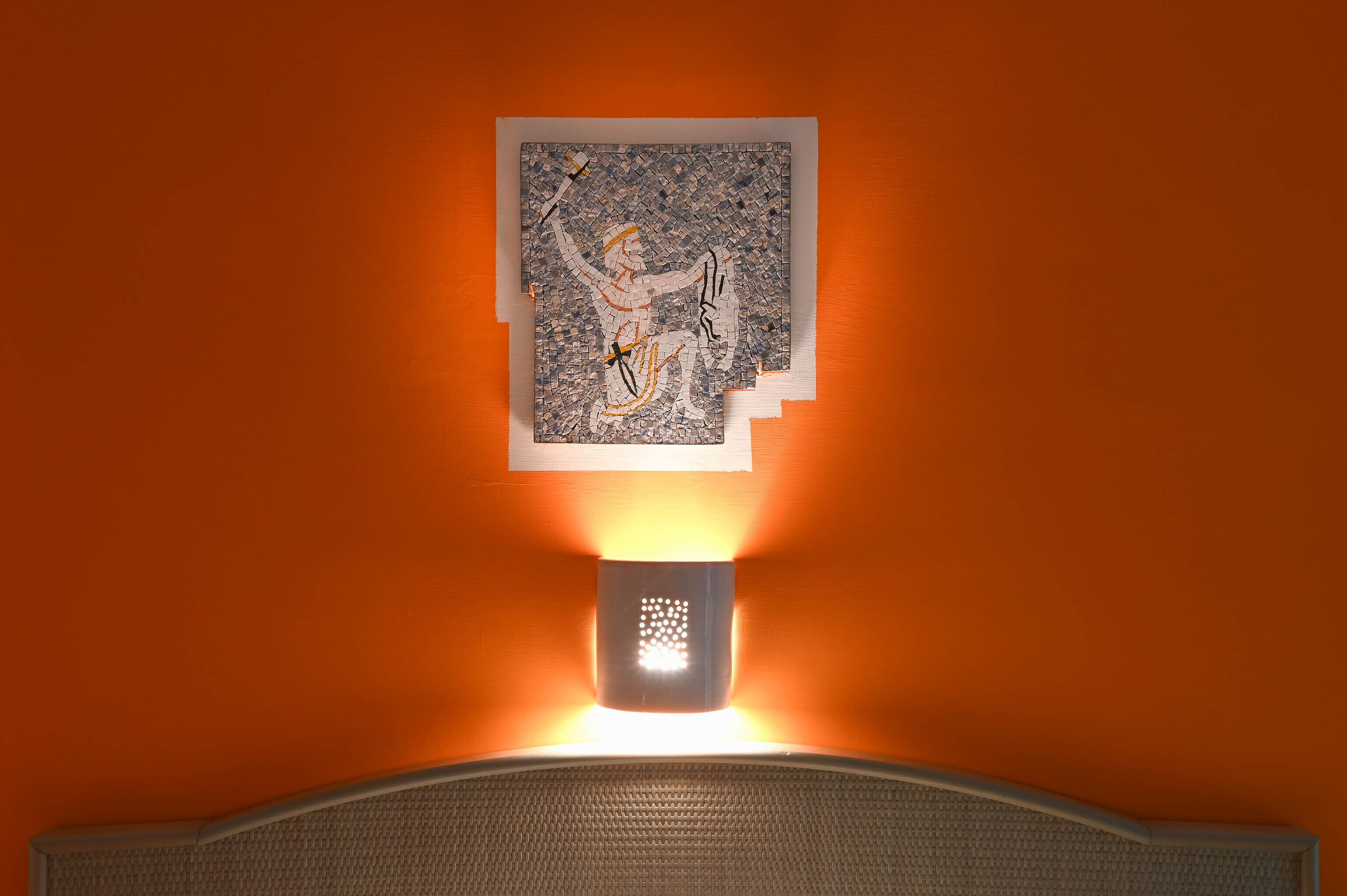 A wall-mounted artwork with a light fixture below it.