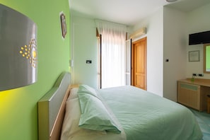 Een slaapkamer met een bed, nachtkastje, spiegel en deur.