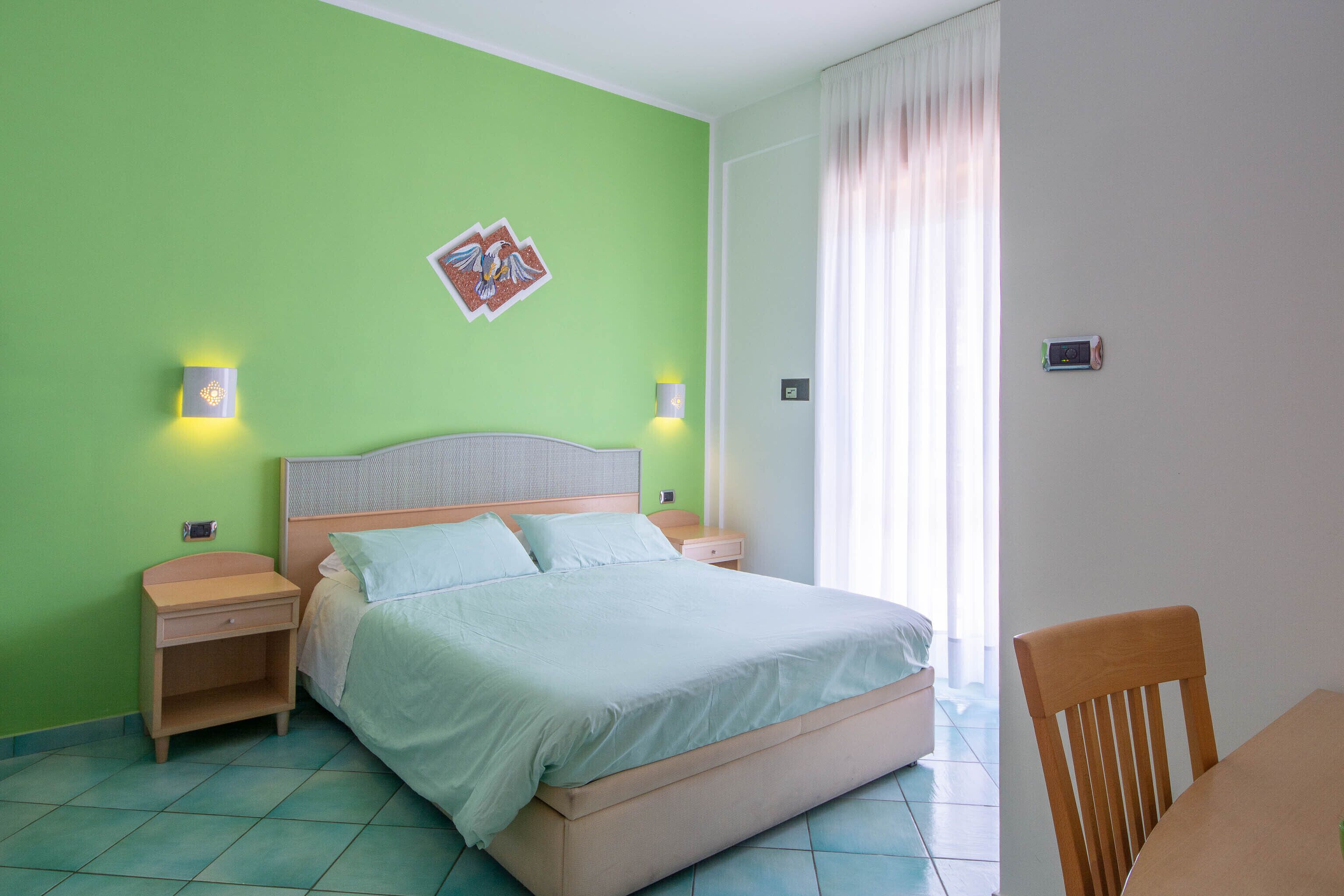 Ein Schlafzimmer mit einem Bett, zwei Nachttischen, einem Beistelltisch, einem Holzstuhl und einem Fenster mit Vorhängen.