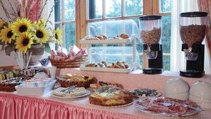 Ein reichhaltiges Buffet mit verschiedenen Speisen, darunter Gebäck, Fleisch und Kuchen, vor einem Fenster mit Blick auf Bäume.