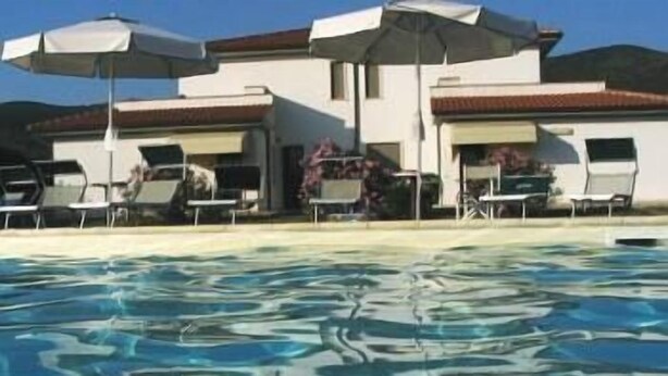 Ein Schwimmbecken mit klarem Wasser, umgeben von Liegestühlen und Sonnenschirmen.