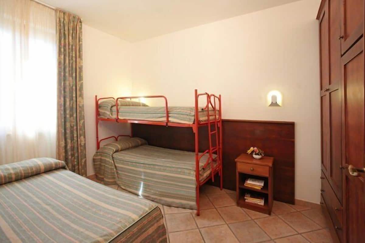 Ein Zimmer mit zwei Etagenbetten, einem kleinen Nachttisch mit Lampe und einem Kleiderschrank.