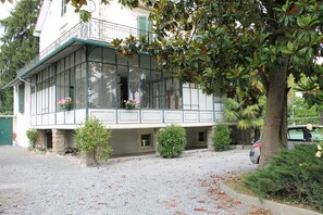A two-story building with a balcony, a gravel driveway, and a parked car.