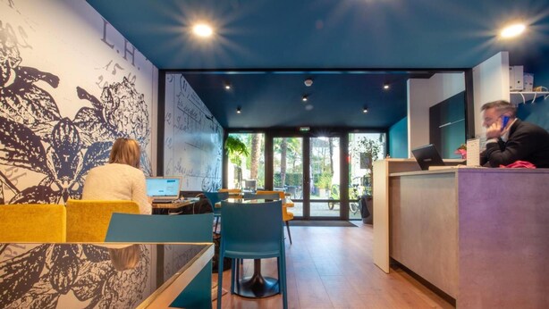 A modern interior with a reception desk, seating area, and a mural on the wall. - Hôtel Montilleul (Pau)