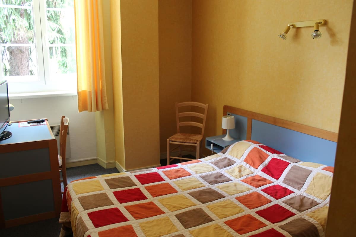 A bedroom with a bed, a desk, a chair, and a window with curtains.