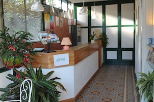 Zona de recepción de un hotel con un mostrador de madera, un cartel que dice "HOTEL DE LOUVRE" y diversas plantas.
