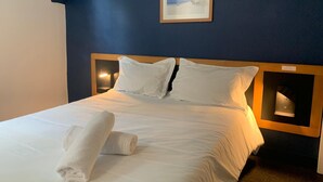 A neatly made bed with white linens and pillows, a rolled towel on the bed, and a framed picture on the wall. - Hôtel Montilleul (Pau)