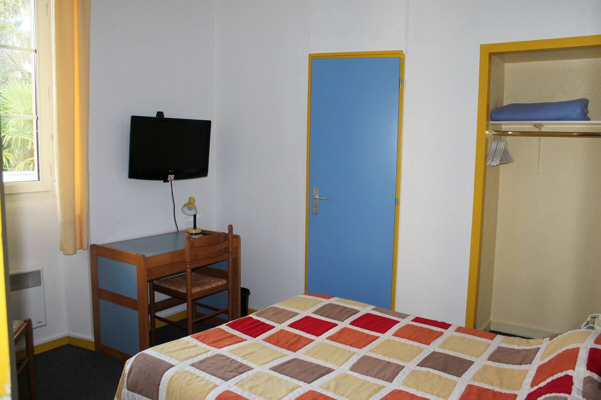 A bedroom with a bed, a desk, a chair, a television, and a wardrobe.