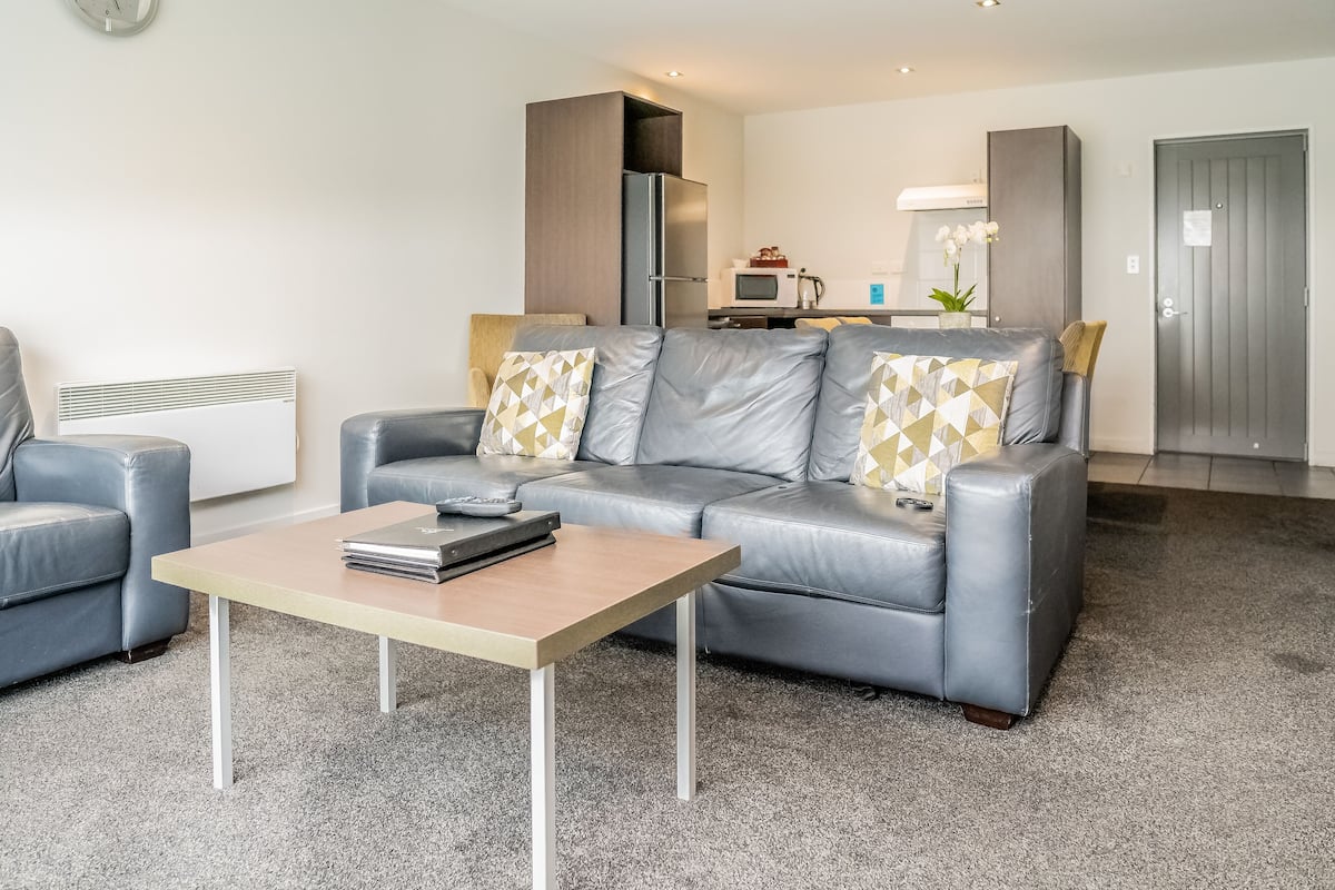 A modern living room with a grey leather sofa, a wooden coffee table, and a grey carpet.