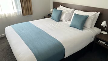A neatly made bed with white and blue bedding, a bedside lamp, and a nightstand with a phone.