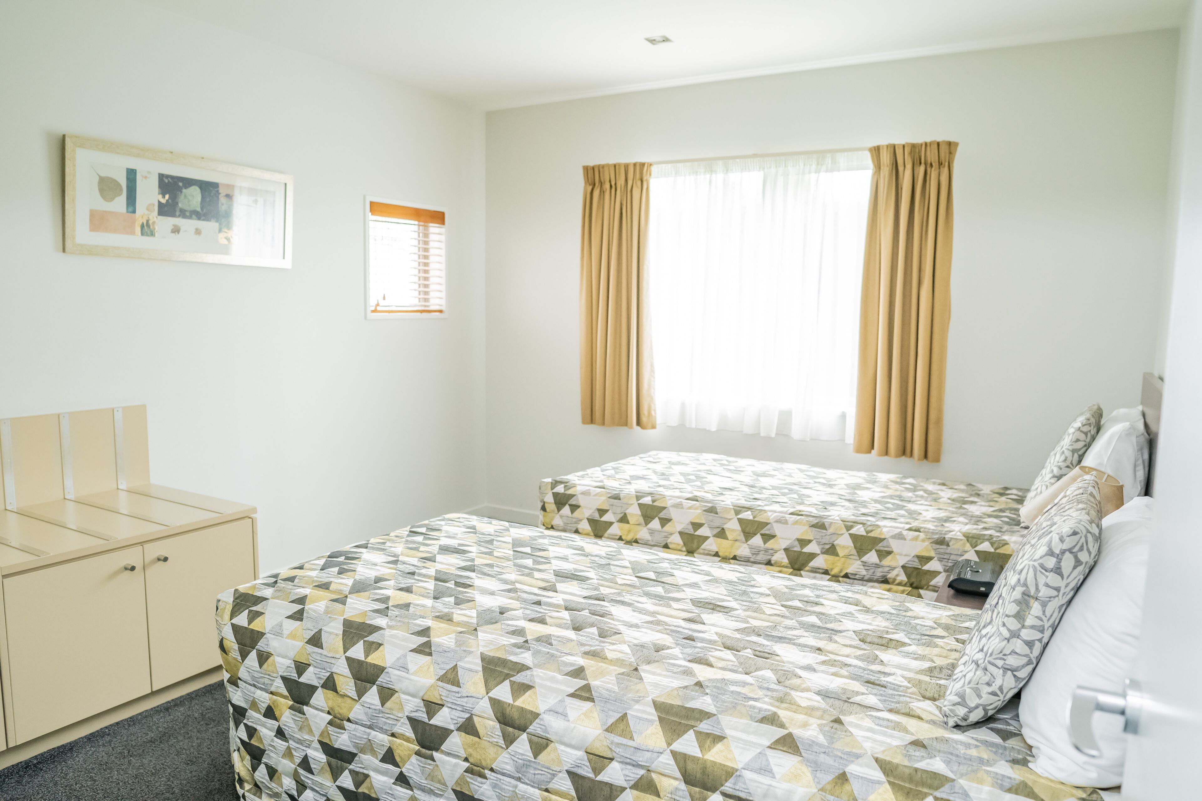 A hotel room with two beds, a small desk, and a window with curtains.
