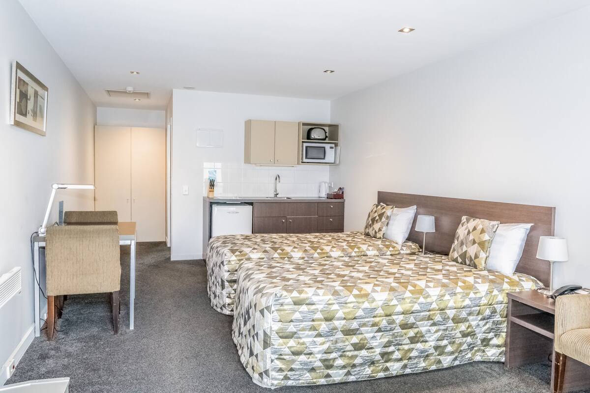 A hotel room with a bed, a desk, a chair, a microwave, and a small kitchenette.