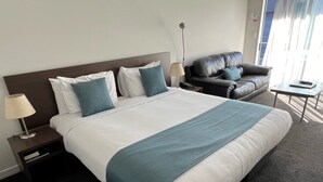 Una habitación de hotel con una cama grande, un sofá, una mesita y una lámpara.