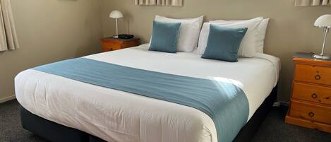 Una cama bien hecha con una colcha azul y blanca, una mesita de noche de madera con una lámpara y un aparador con cajones.