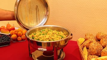 A buffet table with a variety of food items including fruits, a large pot of food, and bread rolls.