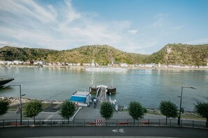 A ferry dock with a boat, a pedestrian bridge, and a view of hills and buildings across the water.