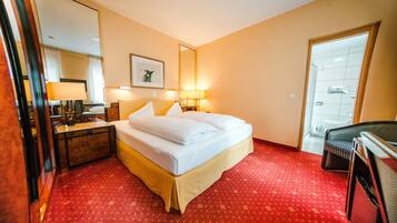 A hotel room with a bed, bedside tables, lamps, a mirror, a framed picture, and a red carpet.