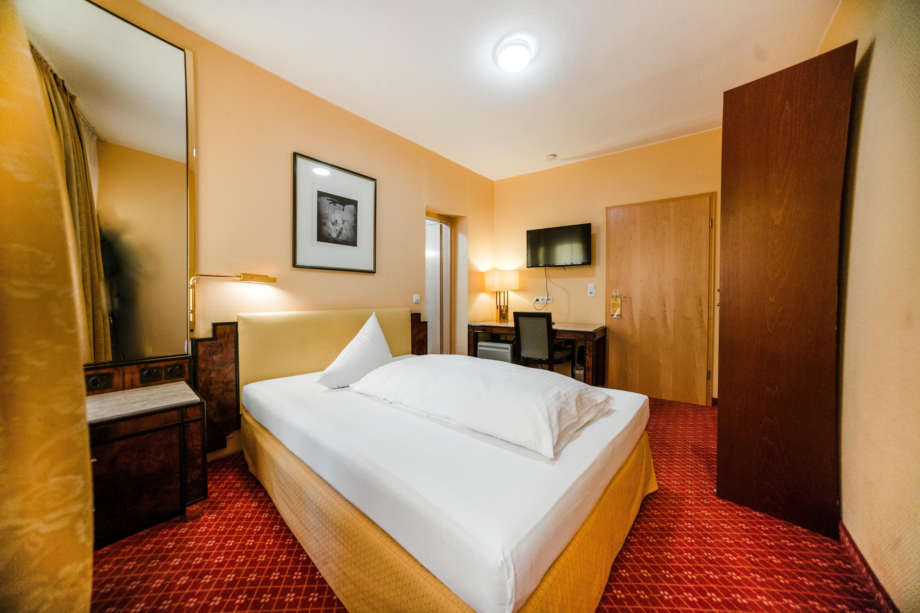 Une chambre d’hôtel avec un grand lit, un bureau avec une chaise, un téléviseur fixé au mur et une porte en bois.