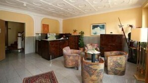 Un vestíbulo con una recepción, dos sillones, una mesita de centro y una alfombra estampada.