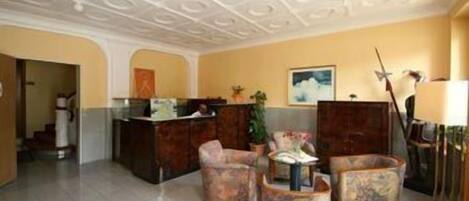 A lobby with a reception desk, two armchairs, a coffee table, and a patterned rug.