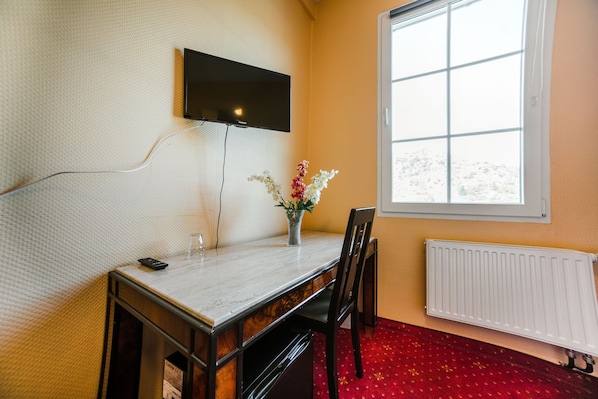 Una habitación con un televisor montado en la pared, un florero con flores sobre una mesa, una silla y una ventana que ofrece vistas de nieve.