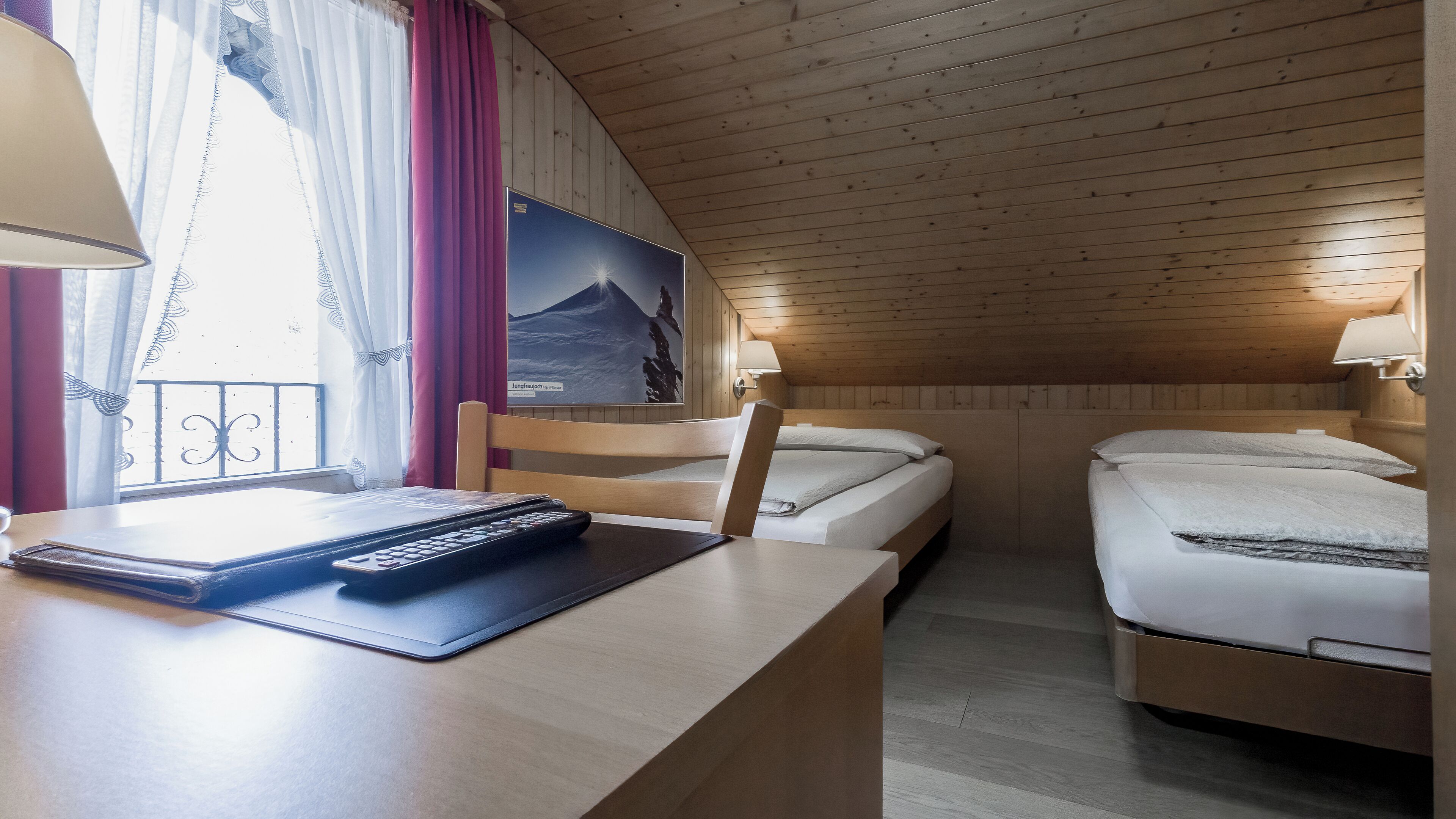 Une chambre confortable avec deux lits, un bureau avec une lampe et une fenêtre avec des rideaux.