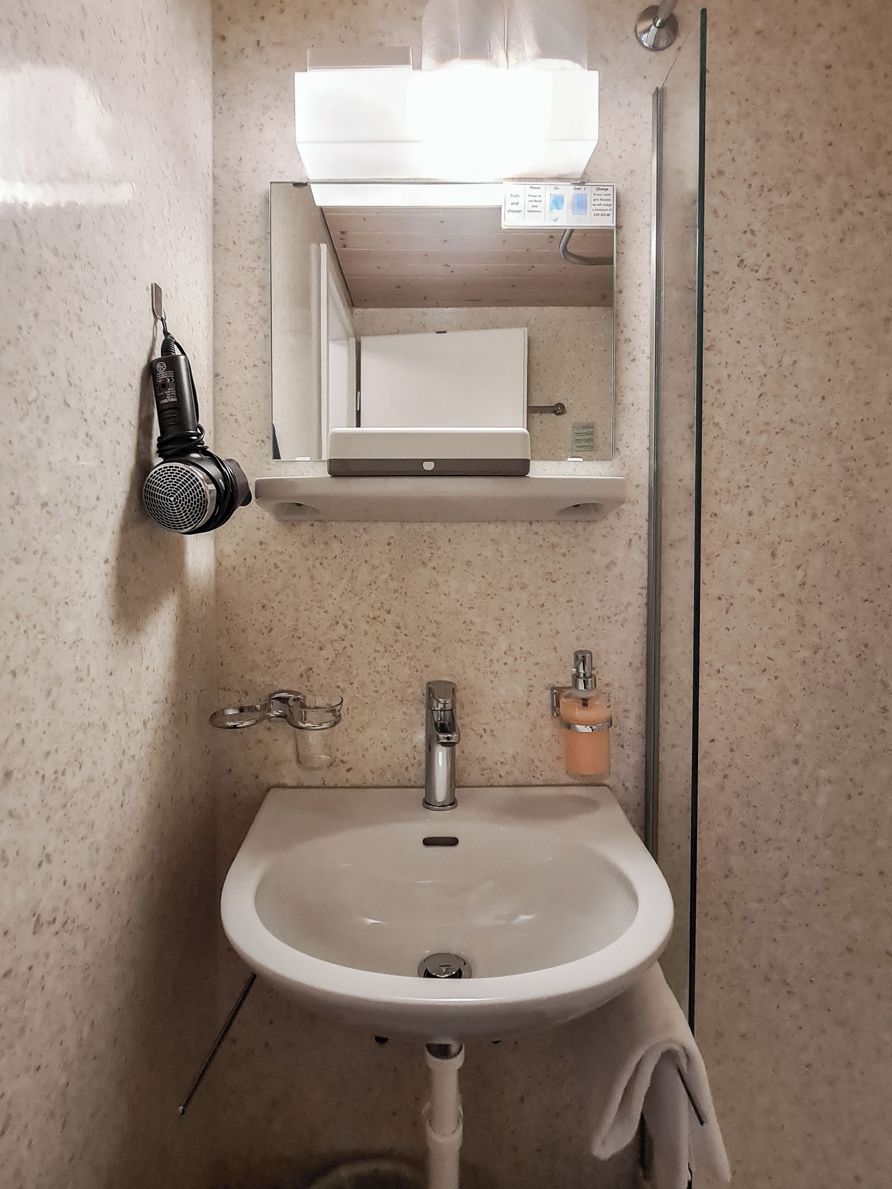 A bathroom with a white sink, a mirror, a towel, and a shower head.