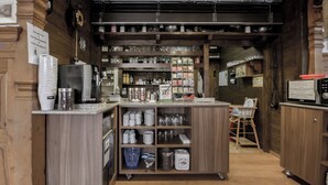 A kitchen area with wooden cabinets, a coffee machine, and shelves stocked with glassware and kitchen utensils. - Hotel Rössli (Unterseen)